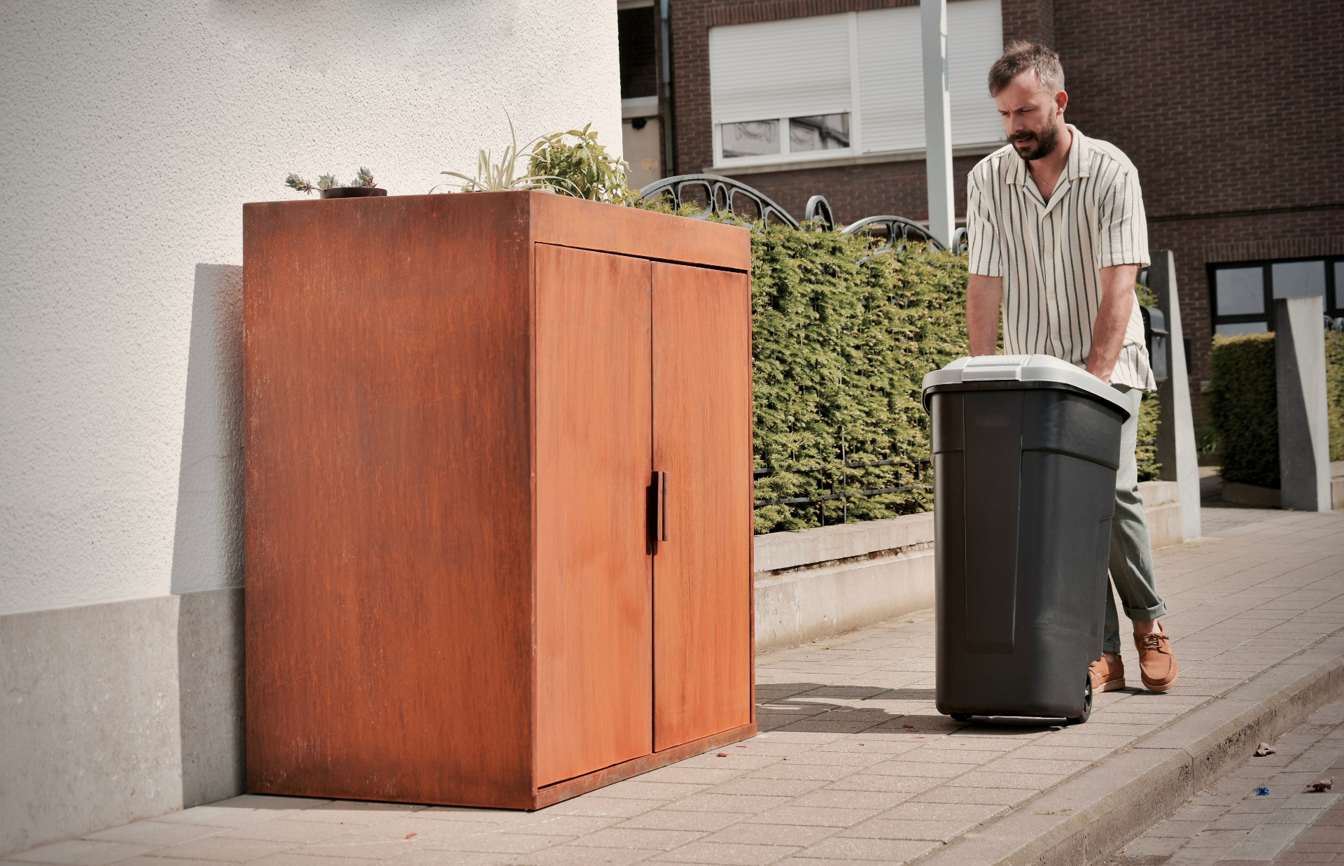 Bewoner rolt zijn afvalcontainer terug in de cortenstalen kast op maat